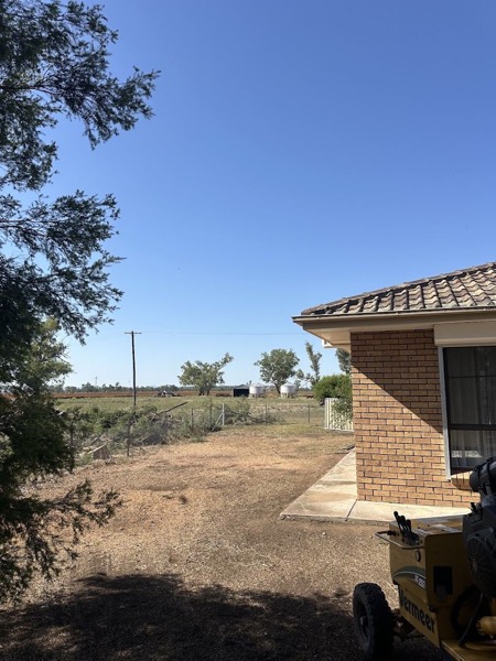 Bare ground beside a brick house with open paddock beyond the fence