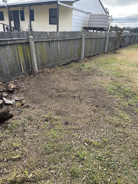 A cleared strip of soil running along a timber paling fence