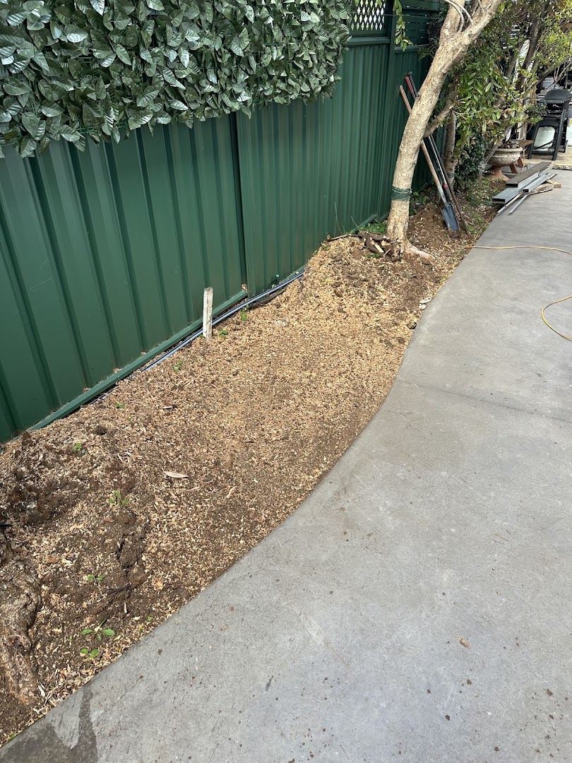A narrow cleared strip of soil between a Colorbond fence and a concrete path